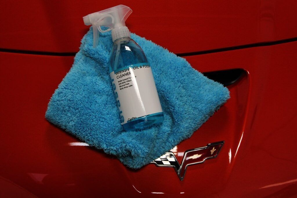 Blue microfiber towel and spray bottle on the hood of a red Corvette.
