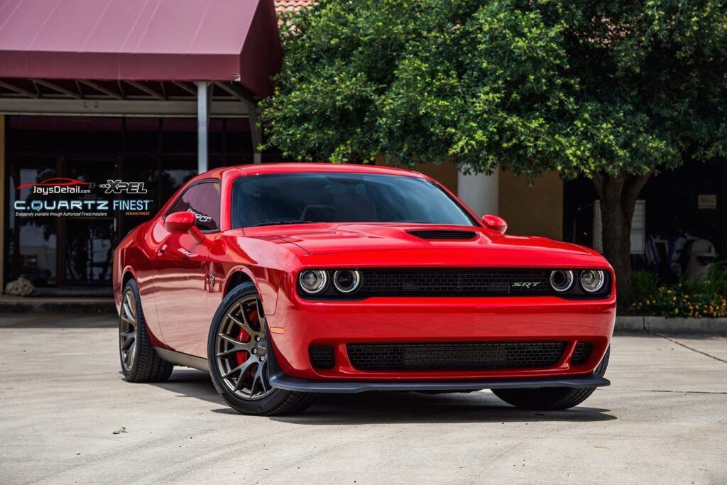Red Dodge Challenger parked in front of a building with trees; a muscle car.