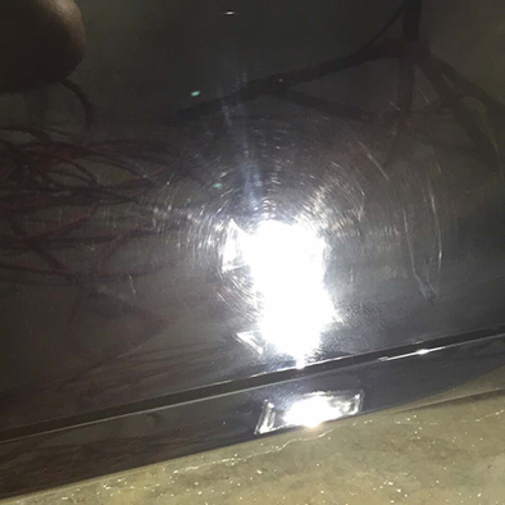 Black car surface with swirl marks, illuminated by a bright light, showing scratches.