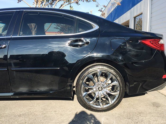 Black sedan with chrome wheels, showing scratches along the side, parked outside a building.