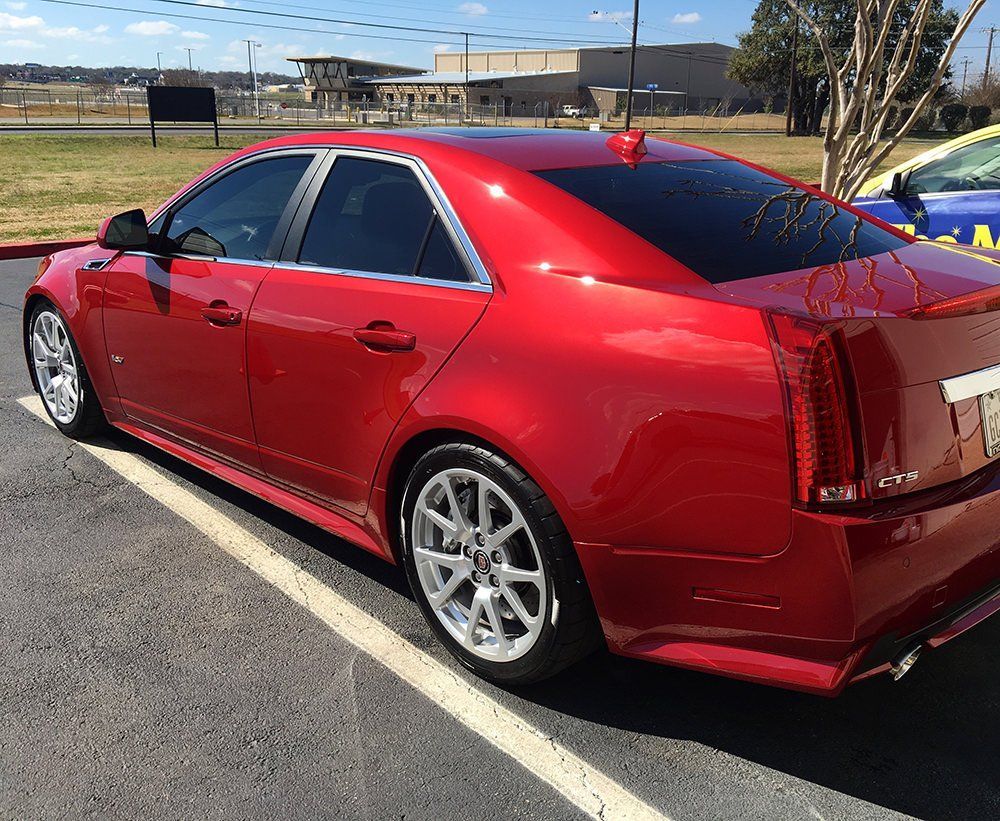 Red Cadillac CTS sedan parked in a parking lot on a sunny day.