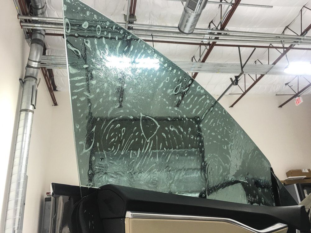 Tinted car window being prepared in a shop, with visible water and film.