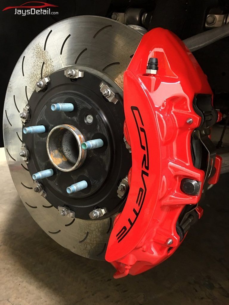 Red Corvette brake caliper on a slotted rotor, blue lug nuts, in a shop setting.