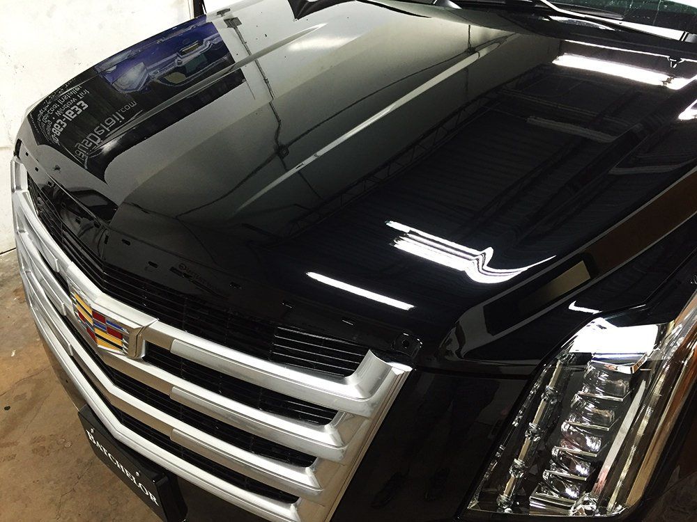 Black Cadillac SUV hood with shiny finish, chrome grille and headlights.