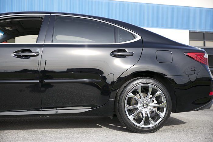 Black Lexus sedan with tinted windows, parked outside with a blue building in the background.