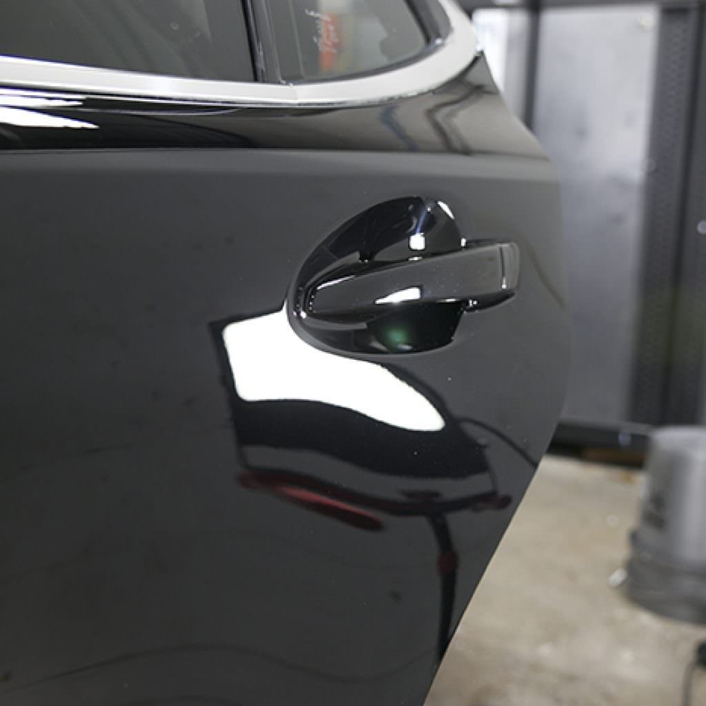 Black car door with shiny black handle, reflecting light.