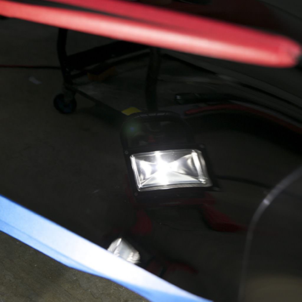 Shiny, black car panel with a reflective, square light fixture; blue and red tape visible.