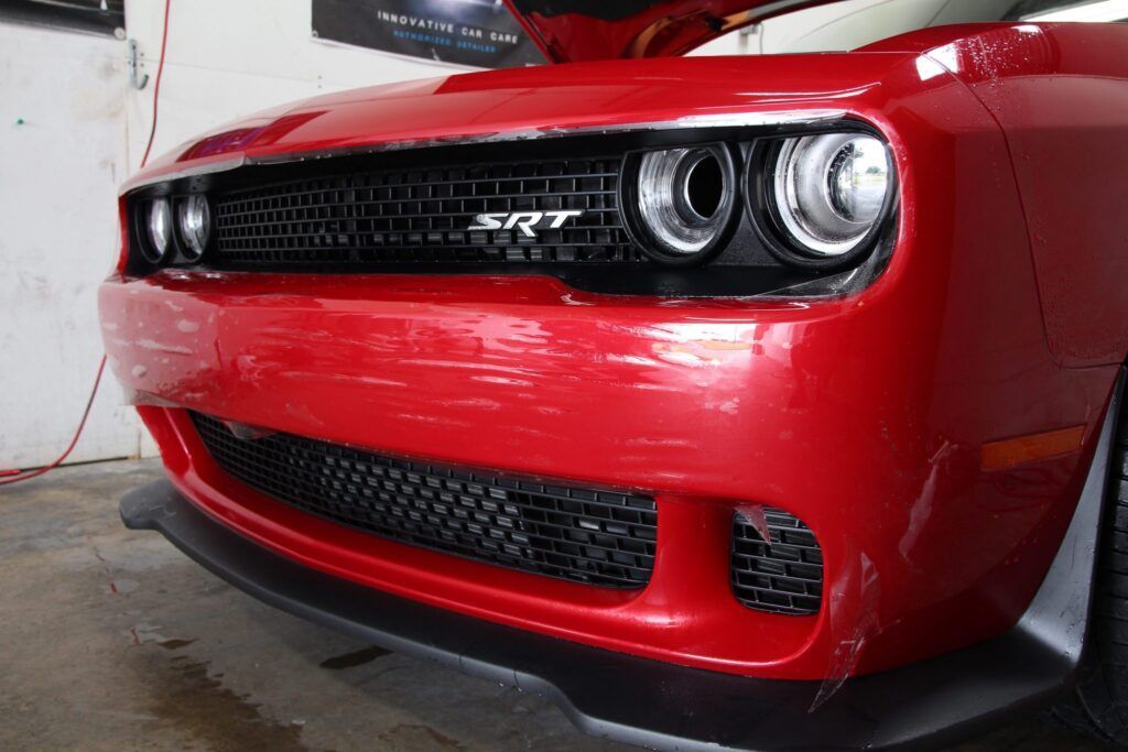 Red Dodge Challenger's close-up view. Grille, SRT emblem, and headlights are visible.