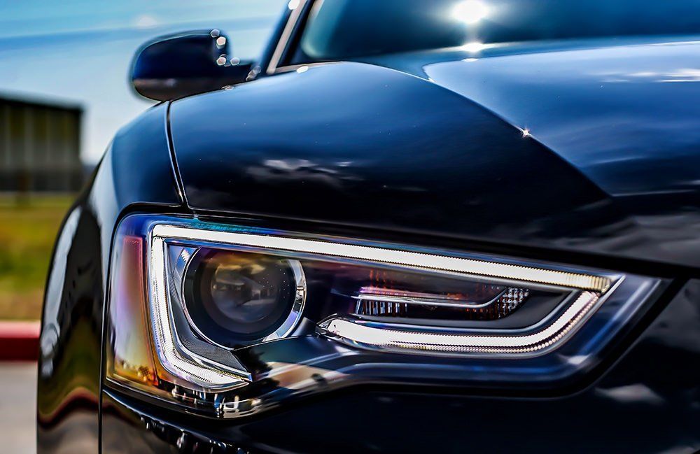 Close-up of a black car's headlight, reflecting sunlight.