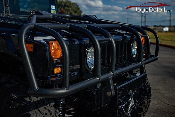 Black Hummer H1 front view with a black brush guard, orange and white lights, and large tires.