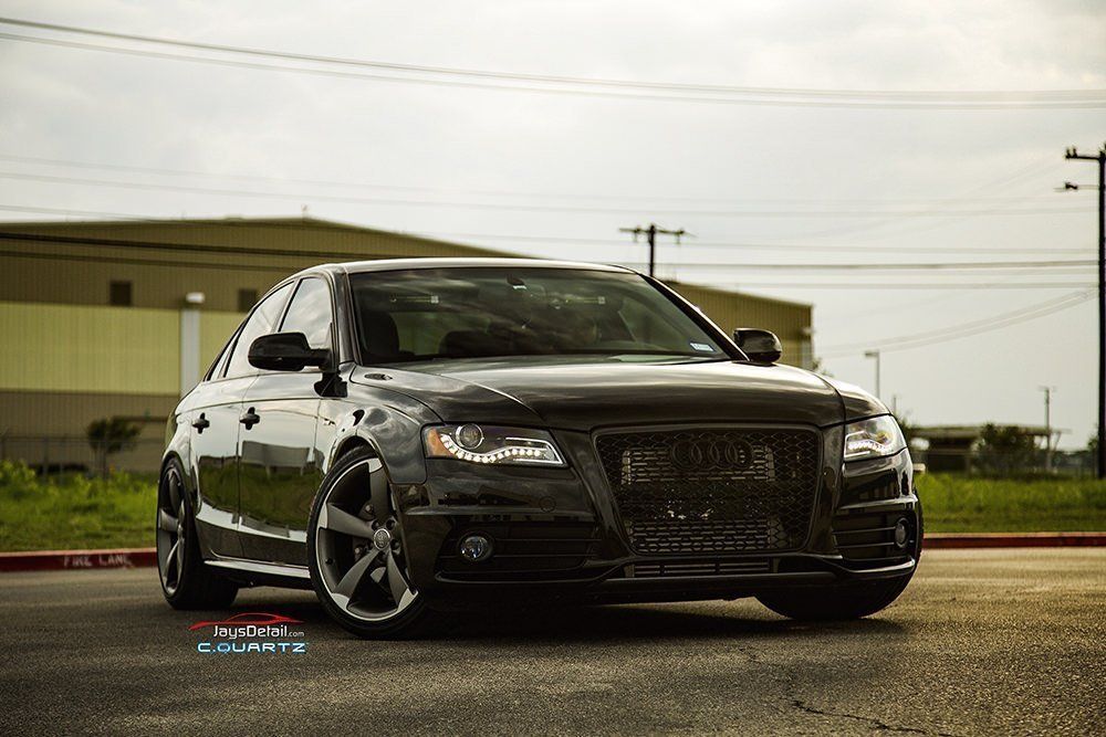 Black Audi sedan with custom grill, dark rims, parked on asphalt.