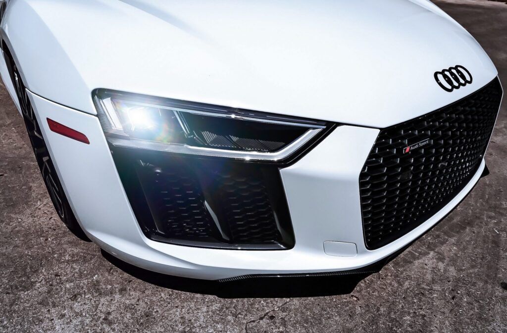 White Audi R8 sports car's front with a bright headlight and the Audi logo.