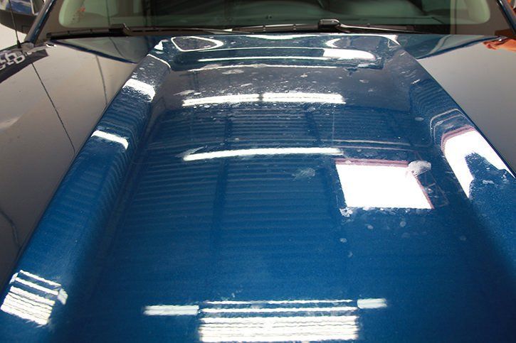 Blue car hood reflecting overhead lights.