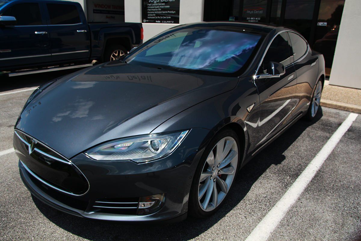Dark gray Tesla parked next to a building, reflecting the sky in the windshield.