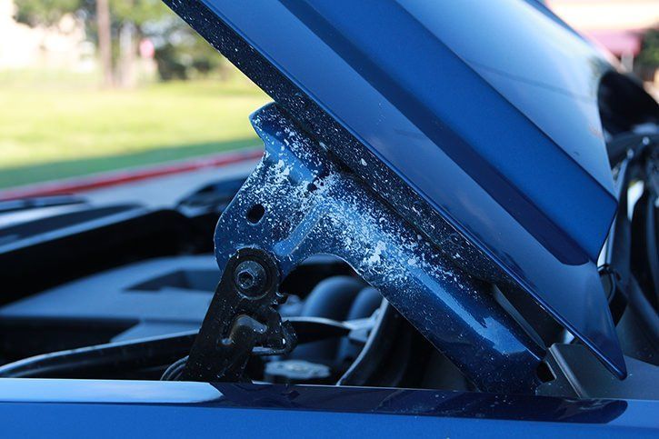 Blue car hood open, showing hinges with white residue.