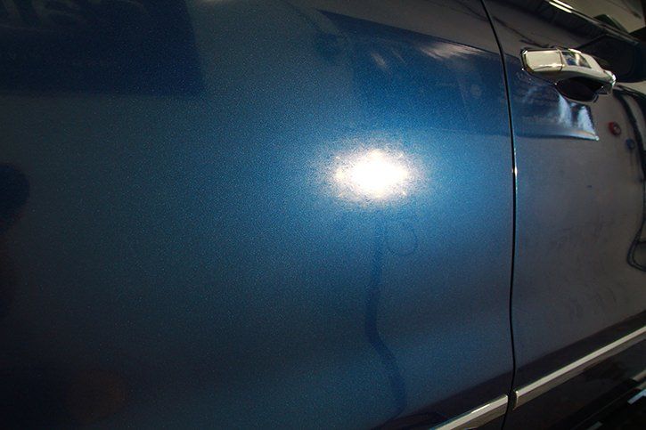 Blue car door with metallic paint reflecting light.