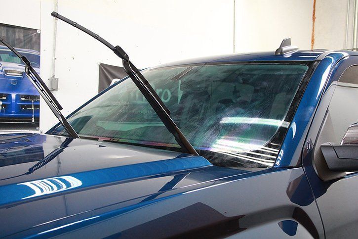 Blue truck with windshield wipers cleaning a dirty windshield.