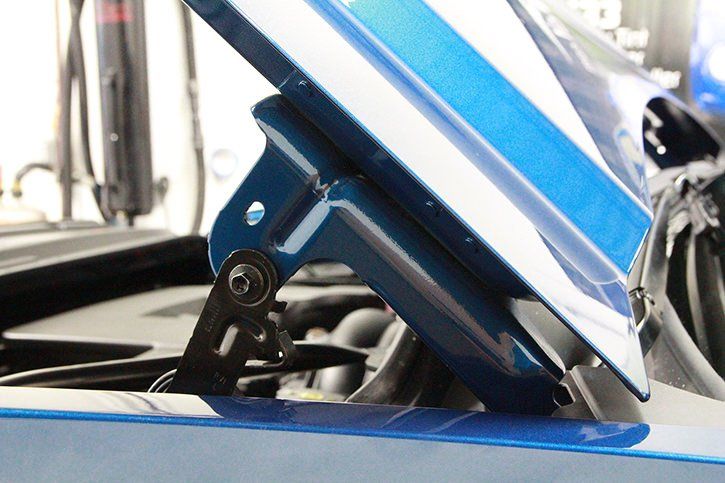 Blue car hood with a black hinge, partially open.