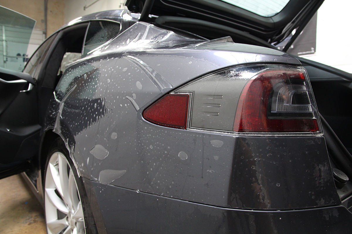 Grey Tesla being fitted with protective film; outdoor, car door open.