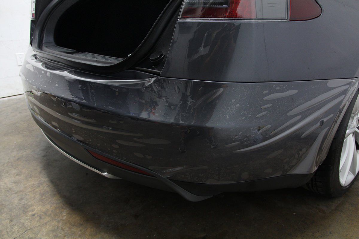 Gray Tesla bumper with clear protective film applied, in a garage.