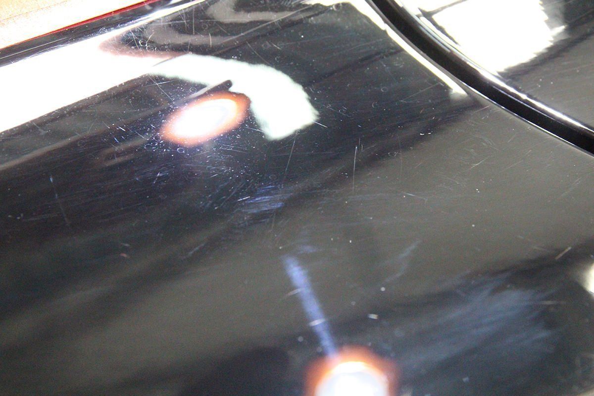 Black car paint with scratches and imperfections, showing light reflections.