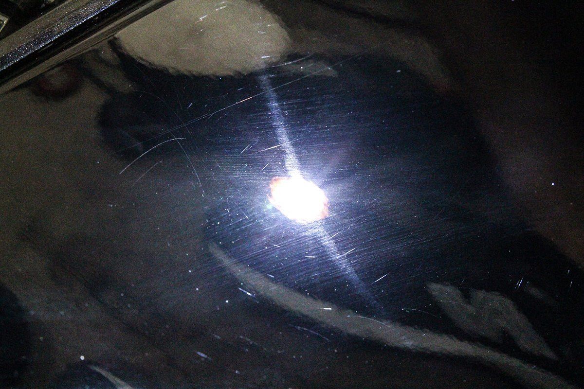 Scratches on black surface, light reflecting and showing imperfections.