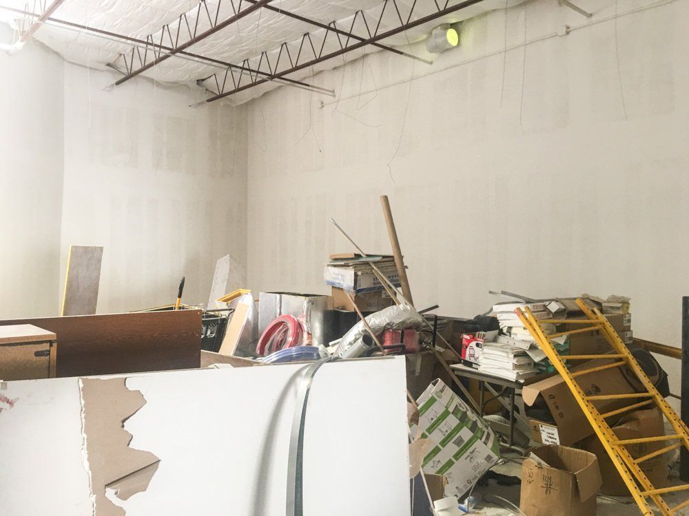 Cluttered, unfinished interior: construction debris, white walls, exposed ceiling beams, yellow ladder.