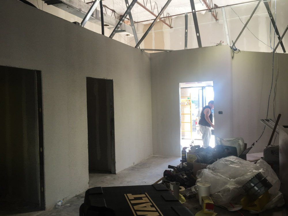 Interior construction in progress: walls, doorways, person in doorway, tools, debris, unfinished ceiling.