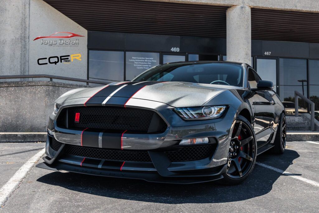 Gray Ford Mustang with racing stripes parked outside a building.