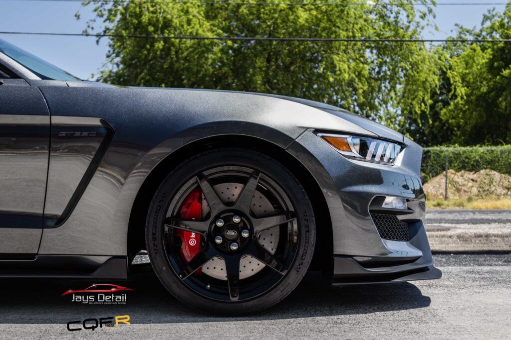 Close-up of a gray Ford Mustang GT350 front end with black rims, red brake calipers, and carbon fiber hood.