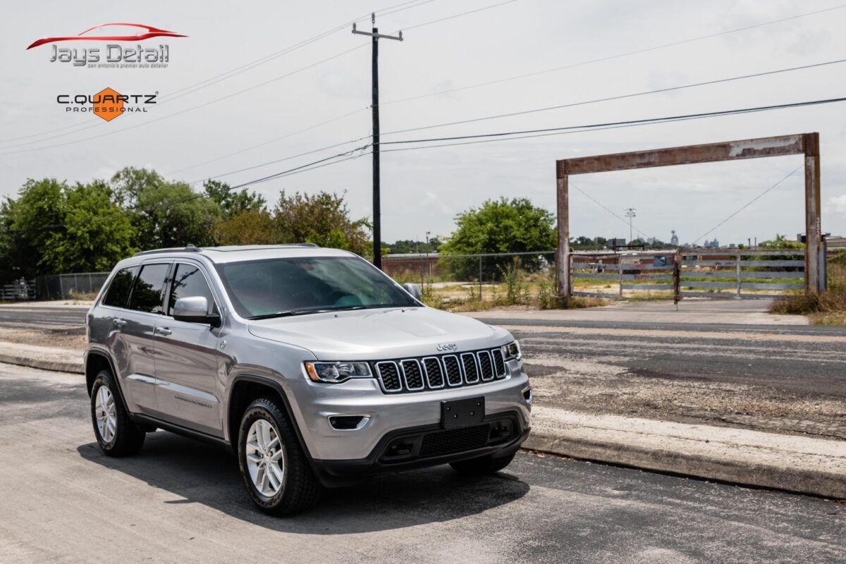 Silver Jeep SUV parked on the side of a road on a sunny day.