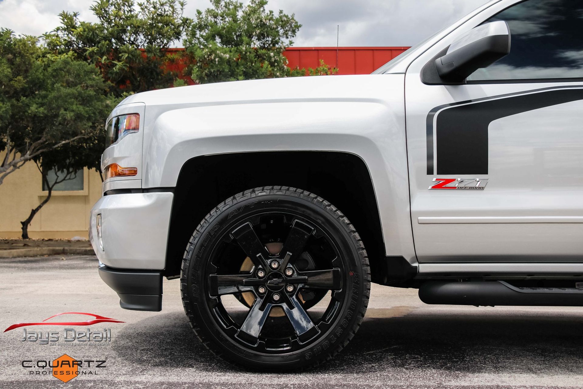 Silver Chevrolet Silverado truck with black wheels and side accent stripe; parked outdoors.