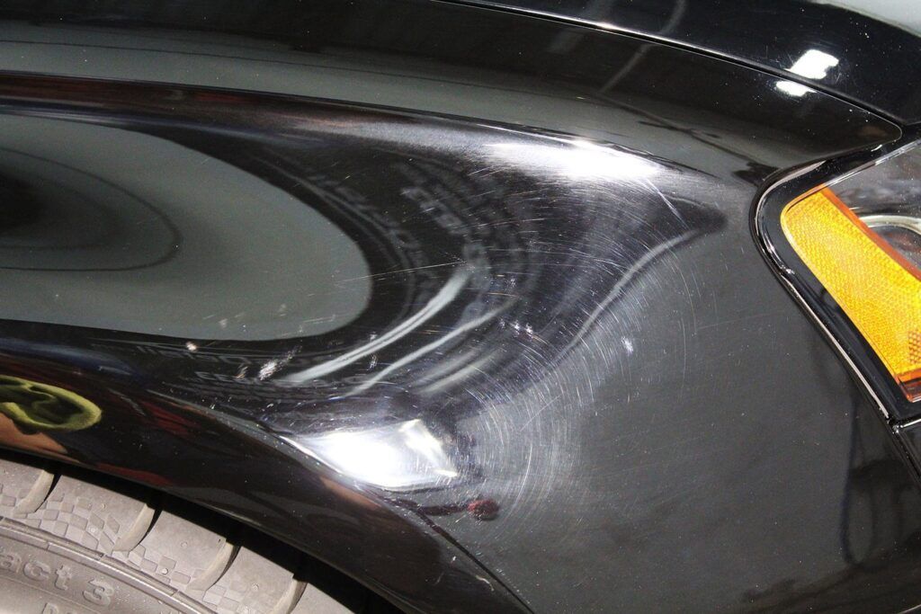 Black car fender with scratches reflecting a bright environment.