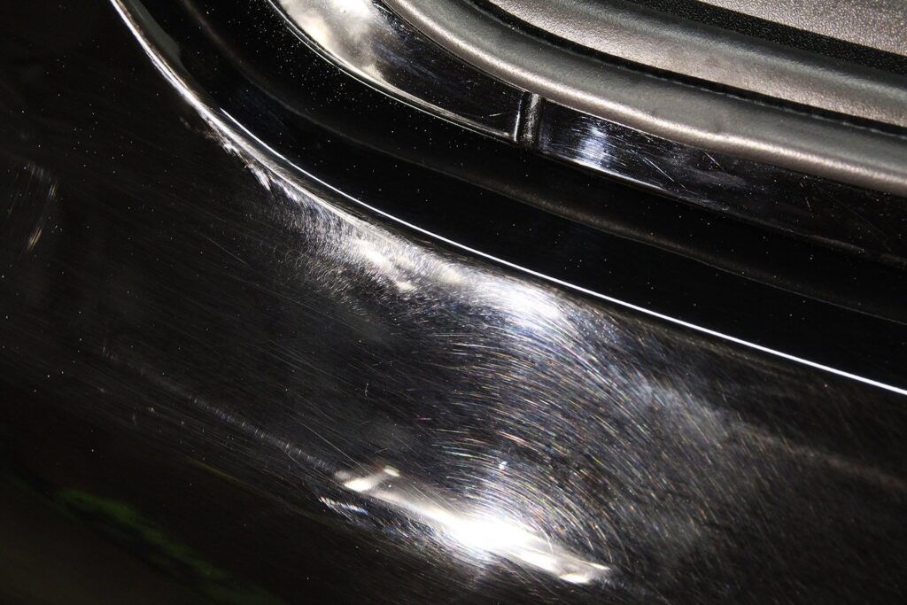 Close-up of shiny, black car paint with visible scratches reflecting light.