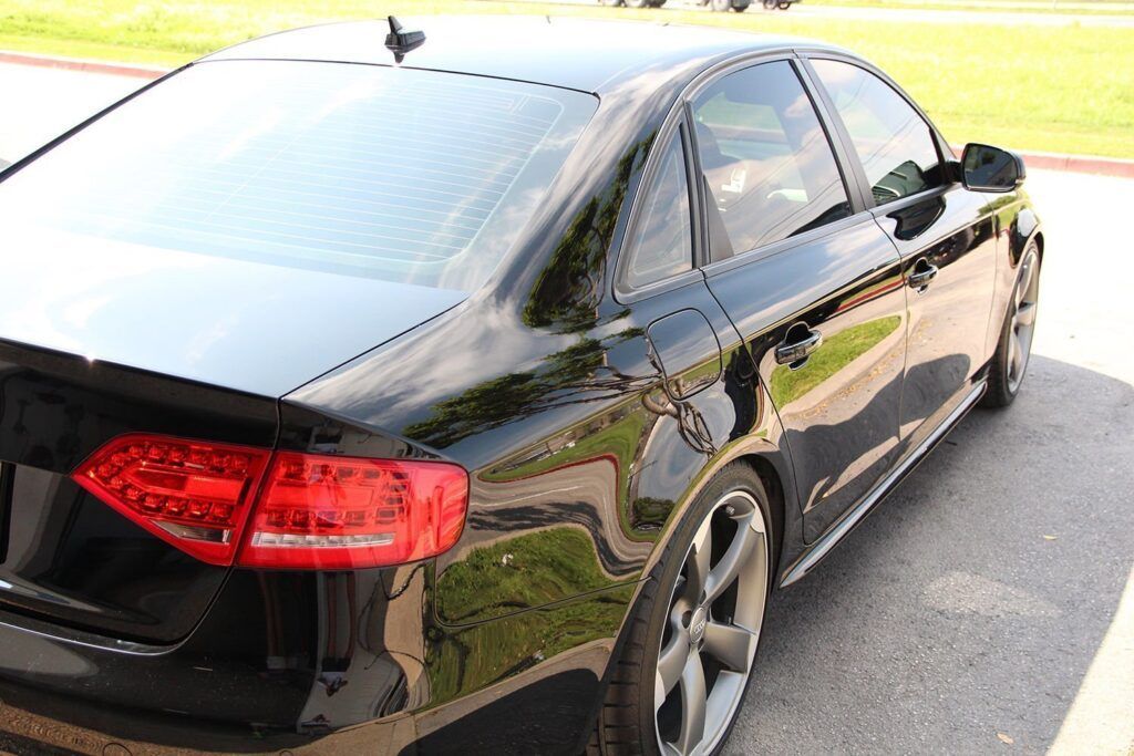 Black Audi sedan parked on pavement, tinted windows, daytime.