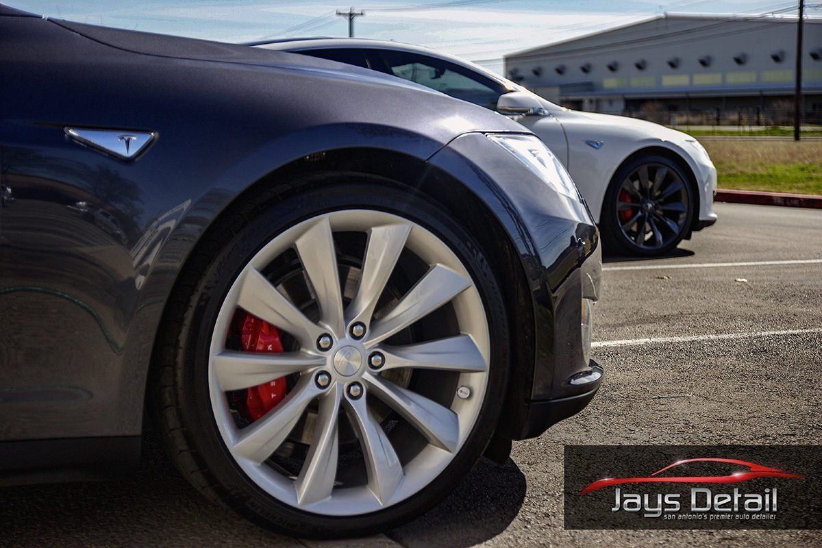 Two Tesla cars, one dark blue, one white, parked outside with red brake calipers.