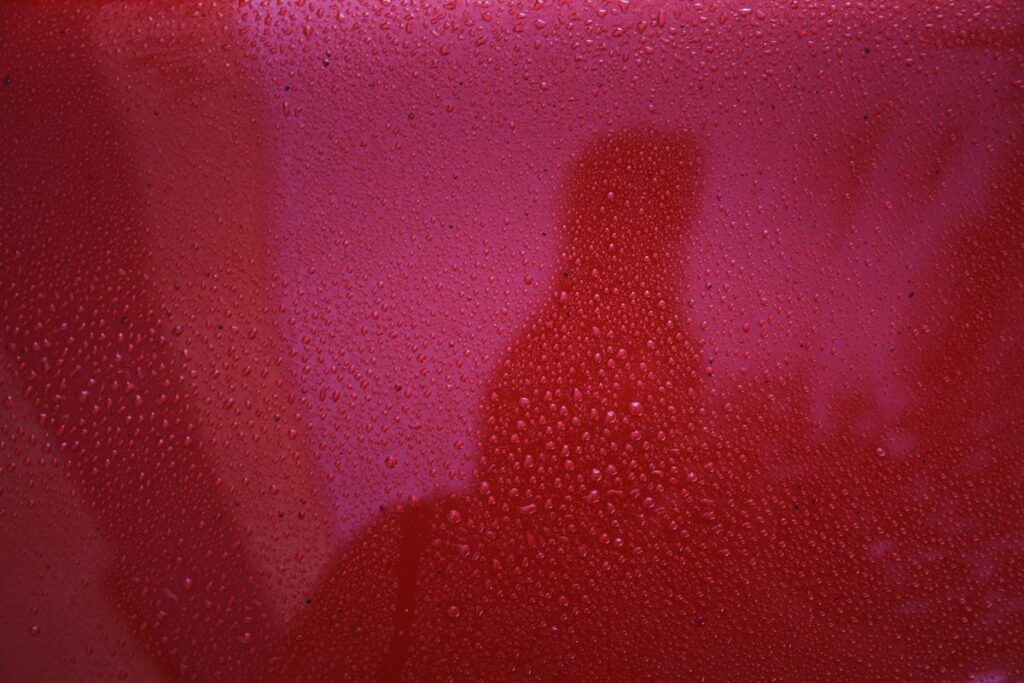 Red surface with condensation, a ghostly figure is faintly visible.