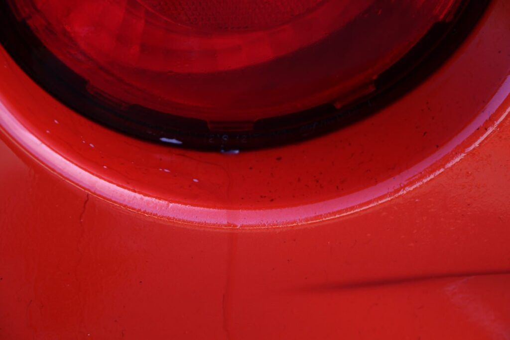 Close-up of a bright red car's taillight and curved body, showing details like paint and reflection.