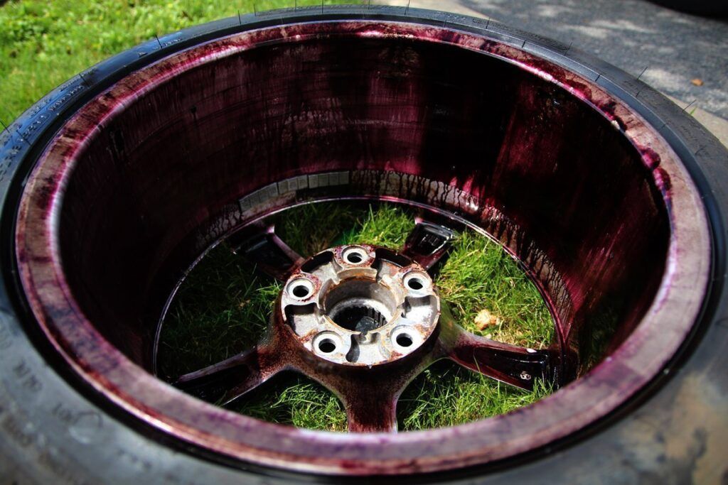 A car wheel, tire removed, revealing a deep red coating on the rim's interior, set on grass.