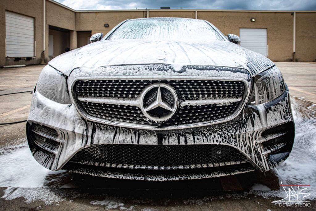 Mercedes-Benz covered in white foam at a car wash, outdoors.