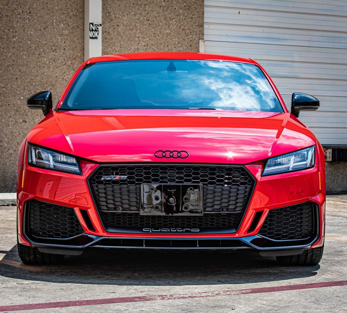 Red Audi TT RS sports car, black grille and accents, parked in front of a building.
