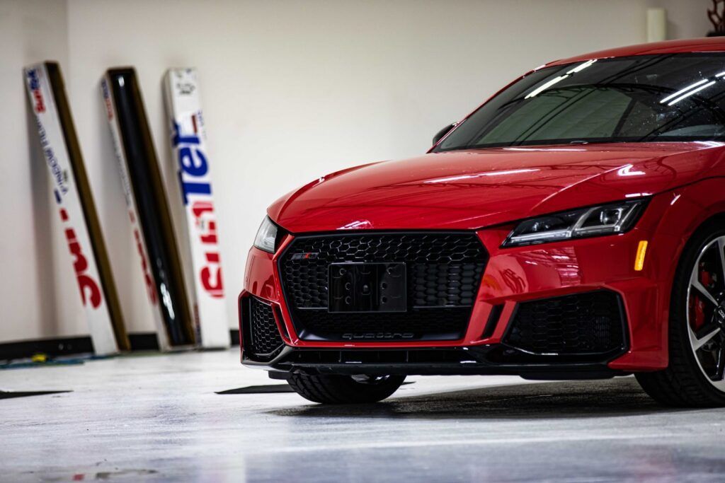 Red Audi TT RS coupe in a garage, with tinting supplies leaning against the wall.
