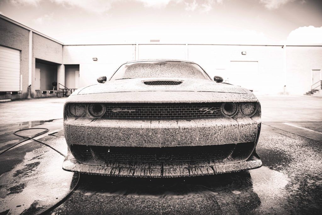 Black and white photo of a Dodge Challenger being foamed with soap. In an industrial setting.