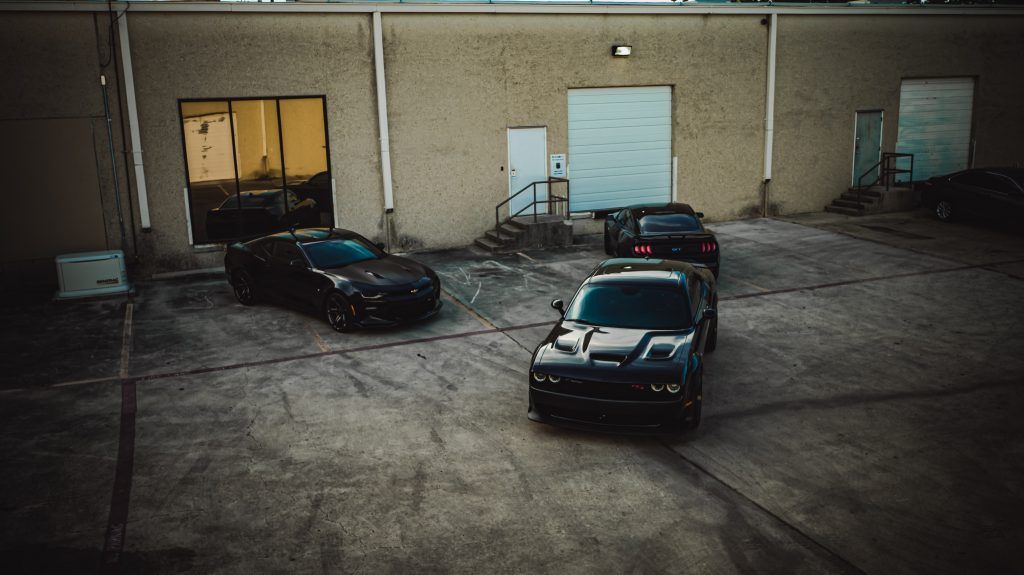 Three dark muscle cars parked in an alleyway, near a building.