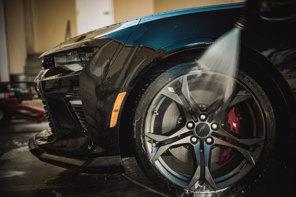 Black car being washed; water spraying on the front wheel and tire.