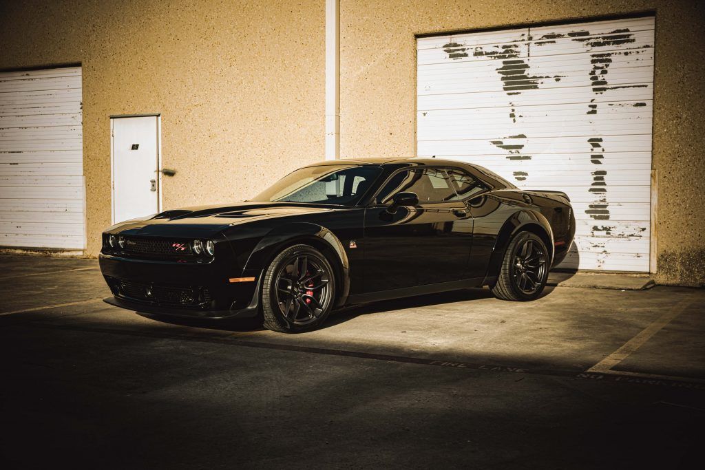 Black Dodge Challenger parked in front of a tan garage door.