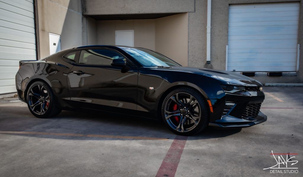 Black Camaro sports car parked near a building with a garage door.