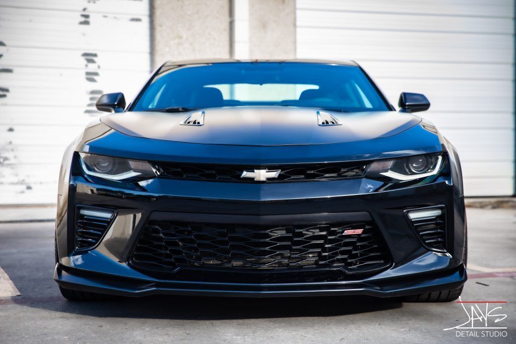 Black Chevrolet Camaro, front view, parked in front of a white building.
