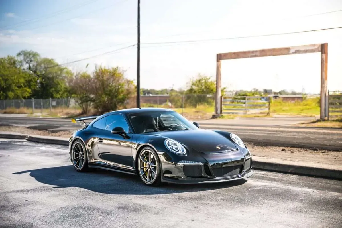 Dark gray Porsche sports car parked in front of a metal arch on a sunny day.
