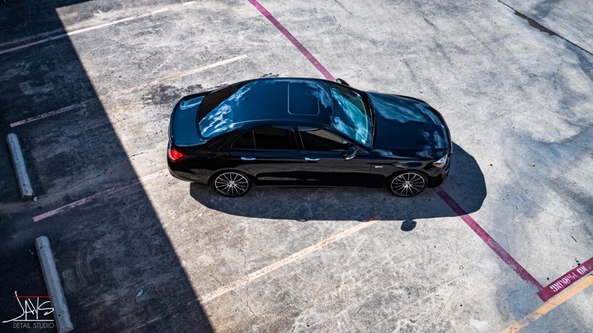 Black car parked in a parking lot, viewed from above, with sunlight casting shadows.